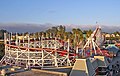 Beyaz, ahşap Santa Cruz Roller Coaster'ın, eğlence parkı yapılarının ve okaliptüs ve palmiye ağaçlarının arka planının akşam fotoğrafı.
