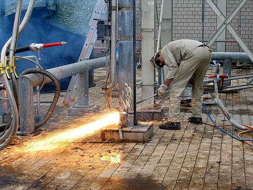 a flame-cutter cuts a steel t-beam during the demolition of an industrial plant