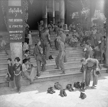 British soldiers remove their shoes at the entrance of Shwedagon Pagoda. To the left, a sign reads "Foot wearing is strictly prohibited" in Burmese, English, Tamil, and Urdu.