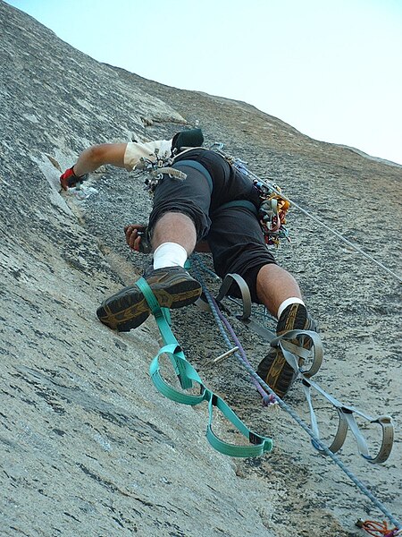 Climber standing in aiders while ascending aid climbing route, The Shield (VI 5.7 A3), on El Capitan