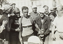 Photographie en noir et blanc d'un cycliste félicité par des spectateurs après l'arrivée de la course.