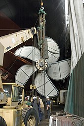 Photographie prise dans un hangar, où l'on voit une hélice en train d'être attachée sur un treuil.
