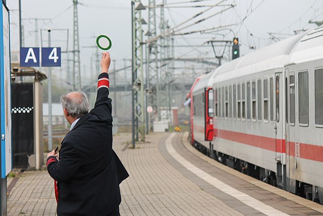 German conductor signaling for the departure of a train. The red armband on his uniform identifies him as a conductor.