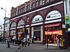 Un bâtiment en briques rouges avec un panneau bleu indiquant "CAMDEN TOWN STATION" en lettres blanches et un panneau rouge indiquant "FIRST CHOICE RESTAURANT" en lettres blanches