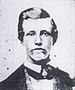 Head and shoulders of a young white man with thick, neatly combed hair, wearing a dark suit and tie.