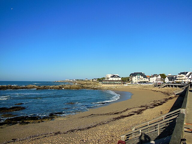 Vue d'une plage sableuse, avec des habitations au fond.