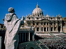St. Peter's Square Crowd in front of a building with a dome photographed from behind a statue on an adjacent rooftop.jpg