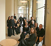 Skidmore (rear, in front of the door) with the Ex Cathedra Choir in the cafe of the Birmingham Town Hall - photographed on 1 March 2008 ExCathedra-BirminghamTownHallCafe-byJamesAshby-20080301.jpg