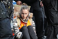 A Letzte Generation activist sits silent at the Massenblockade in Berlin in 2023, surrounded by police, after gluing her hand to the road