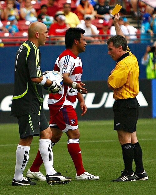 A referee (right) issues a yellow card to a player during a game of association football.