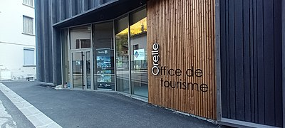 Photographie de la vitrine et de l'entrée de l'office de tourisme d'Orelle, en bois et en verre avec des affiches de promotion.