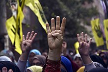 Demonstranten steken hun hand op met het viervingerige R4bia-teken tijdens een mars in Maadi-Caïro op de zes maanden durende herdenking van het gewelddadige optreden tegen aanhangers van de afgezette president Morsi 14-feb-2014.jpg