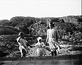 Tre flickor iklädda klänningar håller varandra i handen på strand. Troligen i Fiskebäckskil, Bohuslän - Nordiska Museet - NMA.0054136.jpg