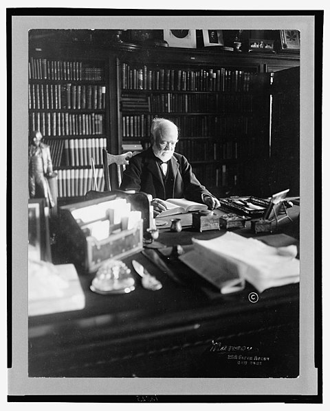 File:Andrew Carnegie, 1835-1919, half length, seated behind desk, looking down at book, facing right; shelves filled with books in background LCCN2005693059.jpg