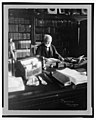 Andrew Carnegie, 1835-1919, half length, seated behind desk, looking down at book, facing right; shelves filled with books in background LCCN2005693059.jpg