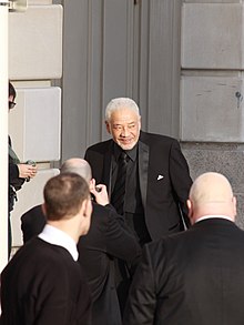 Withers standing before a small crowd in a suit