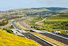 The San Joaquin Hills Toll Road (State Route 73) climbs into the San Joaquin Hills, as seen looking southward from University Hills in Irvine. In the foreground is the tolled Bonita Canyon Drive exit. CA73.jpg