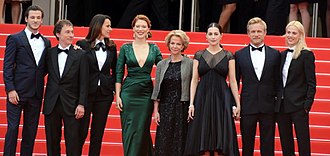 Photographie au format paysage et en couleurs de plusieurs personnes en tenue de gala, posant en souriant sur un tapis rouge.