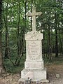 Photo en couleur d'une croix commémorative en pierre au milieu d'un bois.
