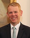 Un bărbat zâmbitor, purtând un costum de afaceri închis la culoare și cravată