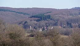 Der Glockenturm des Dorfes und einige Häuser sind von großen bewaldeten Hügeln umgeben.