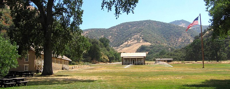 Parade ground at Fort Tejon, California, June 2006. The restored barracks are at left and the commanding officer's quarters are at the center, to the right of and behind which are the stabilized but unrestored officers' quarters. Split rail fences outline the foundations of buildings that have not been reconstructed.