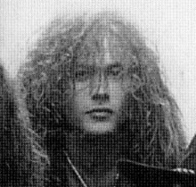 Grainy, black-and-white image of Caucasian, long-haired male looking directly into camera