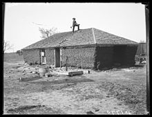 Homme debout sur le toit d'une maison de terre délabrée avec une hache ou un outil similaire