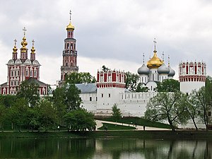 A walled monastery with red and white towers with golden domes