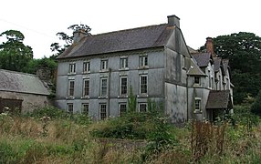 Photo d'un bâtiment de trois étages visiblement à l'abandon, au milieu d'un terrain envahi par la végétation