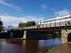 A train crossing a bridge with one stone pier of the bridge in the water of the river