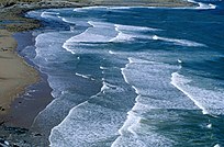 Le onde bordate di schiuma creano un motivo smerlato su una spiaggia sabbiosa in pendenza