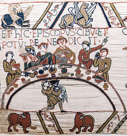 Scène 43 de la Tapisserie de Bayeux représentant Odon, évêque de Bayeux, demi-frère du duc, bénissant le premier banquet que Guillaume le Conquérant et ses barons normands tiennent sur le sol anglais lors de la conquête de l'Angleterre. (définition réelle 2 297 × 2 472)