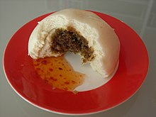 Broken open bakpau showing minced meat filling, served with sweet chili sauce
