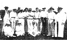 Photo d'un groupe d'hommes habillés en blanc. Neuf hommes sont debout et les trois autres sont assis devant eux.