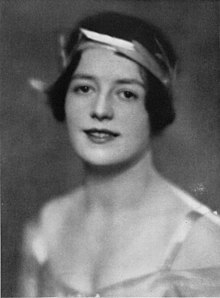 A young white woman with short dark hair, wearing a stylized laurel wreath and a low-cut satiny gown