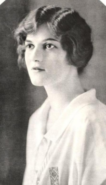 Portrait d'une jeune femme blanche aux cheveux ondulés foncés, vêtue d'un chemisier ou d'une chemise à col blanc