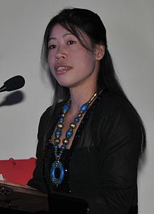 A photograph of Mary Kom looking slightly away from the camera while speaking on a microphone