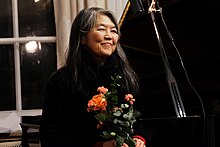 Masako Ohta nach einem Konzert mit einem Blumenstrauß in der Hand, hinter ihr steht ein Flügel