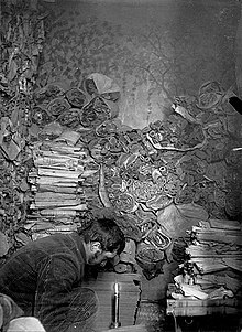 Dans une salle avec de nombreux manuscrits, un homme lit à l'aide d'une bougie.