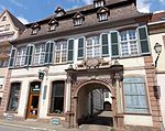 Photographie d'un bâtiment blanc de deux étages avec une arche sculptée en gré rose qui donne sur une cour intérieure.