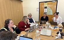 a group of people sitting around a table in front of laptops with ext books around them