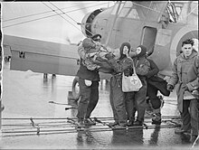 Black and white photograph of men carrying another man from an aircraft