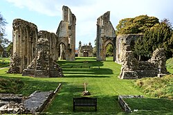 Ruins of church choir and transept on grassy lawn, closely flanked by trees