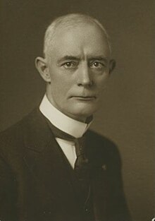 1909 black and white head and shoulders photo of John H. Fraine in suit and tie, facing to his left, looking towards camera
