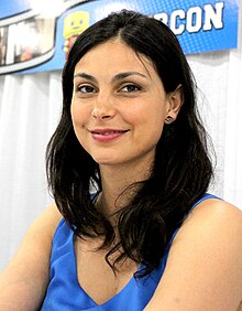 A smiling woman with shoulder-length, dark brown hair and wearing a white blouse looks off to her right