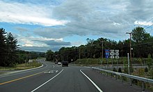 A two-lane paved road curves gently ahead of the viewer in a mostly wooded area under a mostly cloudy sky. There is a left-turn lane immediately ahead and another road leaving at a right angle to the right, going slightly uphill, with steel guardrails on the right. Black and white signs at the right identify the road ahead as "30A", the road to the right as "30", and state that the road ahead will lead the driver to an "88", signed in red, white and blue.