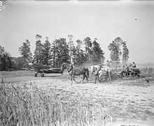 A Spitfire Mark IX of No. 443 Squadron RCAF taxies to dispersal at B-2 Bazenville, alongside a field where French farmers are gathering in the wheat