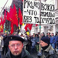 "Russian March" in 2012 in Moscow. An anti-Semitic poster against the background of flags with a nationalist and neopagan symbol "Kolovrat". The poster reads: "Rus' without a Vozhd is like zhyds without a Talmud." Russian March 2012.jpg