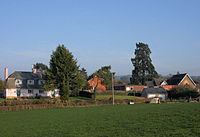 Several houses and school behind fields and hedgerows.